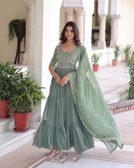 Woman in a green traditional outfit standing in an outdoor setting with plants.