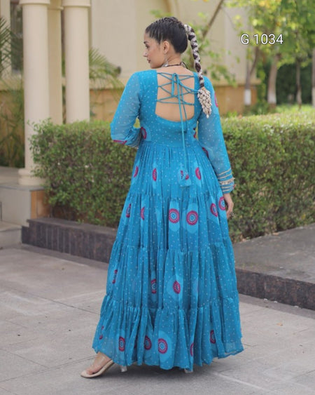 A woman wearing a bright blue tiered maxi dress with circular patterns, shown from the back in an outdoor setting with columns and hedges.