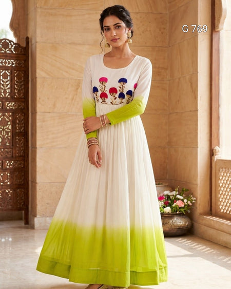 Woman wearing a white and green dress with floral embroidery in a decorative setting.