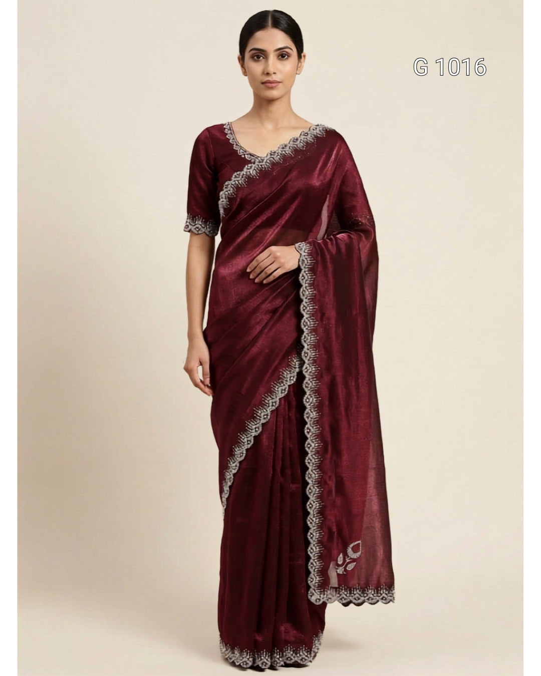 A woman modeling a deep maroon silk saree with silver embroidered borders and a matching embroidered blouse, set against a plain beige background.