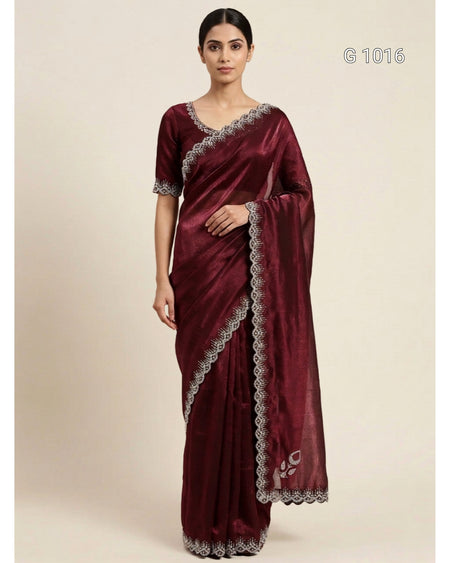 A woman modeling a deep maroon silk saree with silver embroidered borders and a matching embroidered blouse, set against a plain beige background.