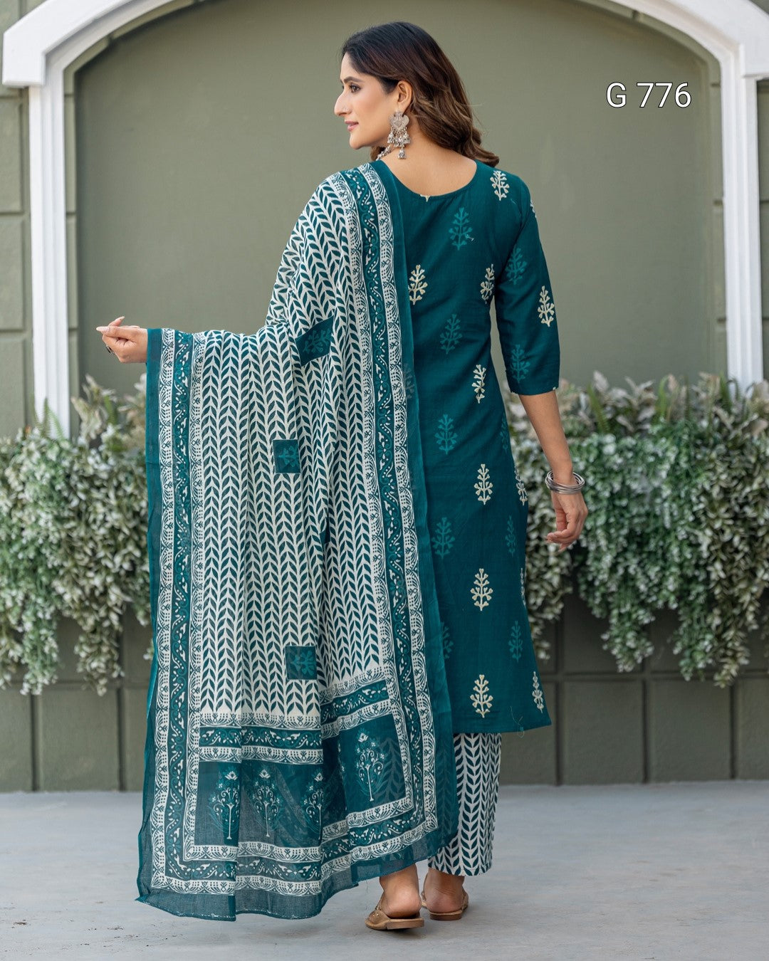 Woman wearing a teal embroidered outfit with a matching dupatta, standing outdoors.