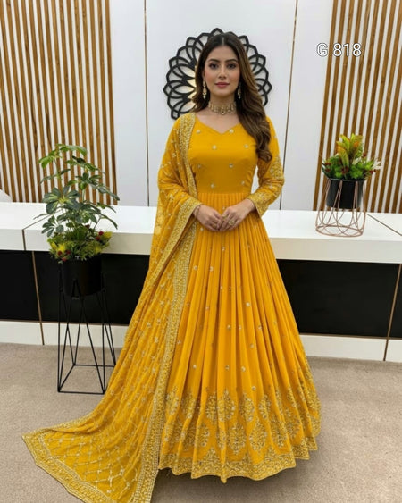 Woman in a yellow traditional outfit standing in a modern interior setting with plants and decor.