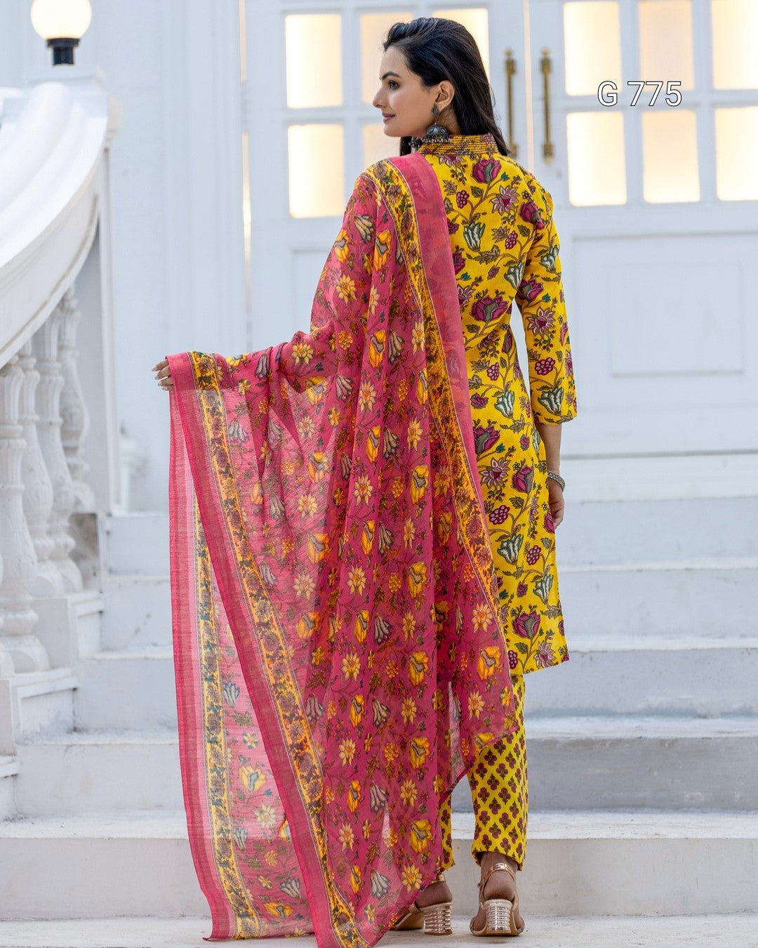 Woman in a yellow and pink traditional outfit standing on a staircase.