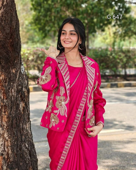 Woman in a bright pink saree with gold embroidery standing outdoors next to a tree.