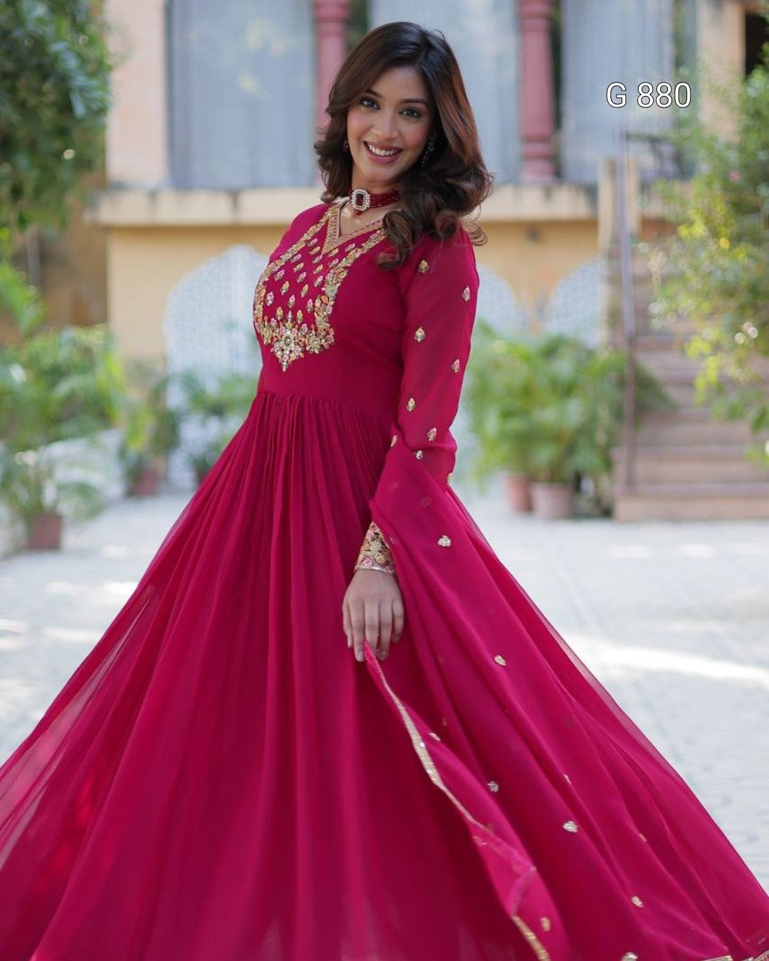 Woman in a red gown with gold embroidery standing outdoors.