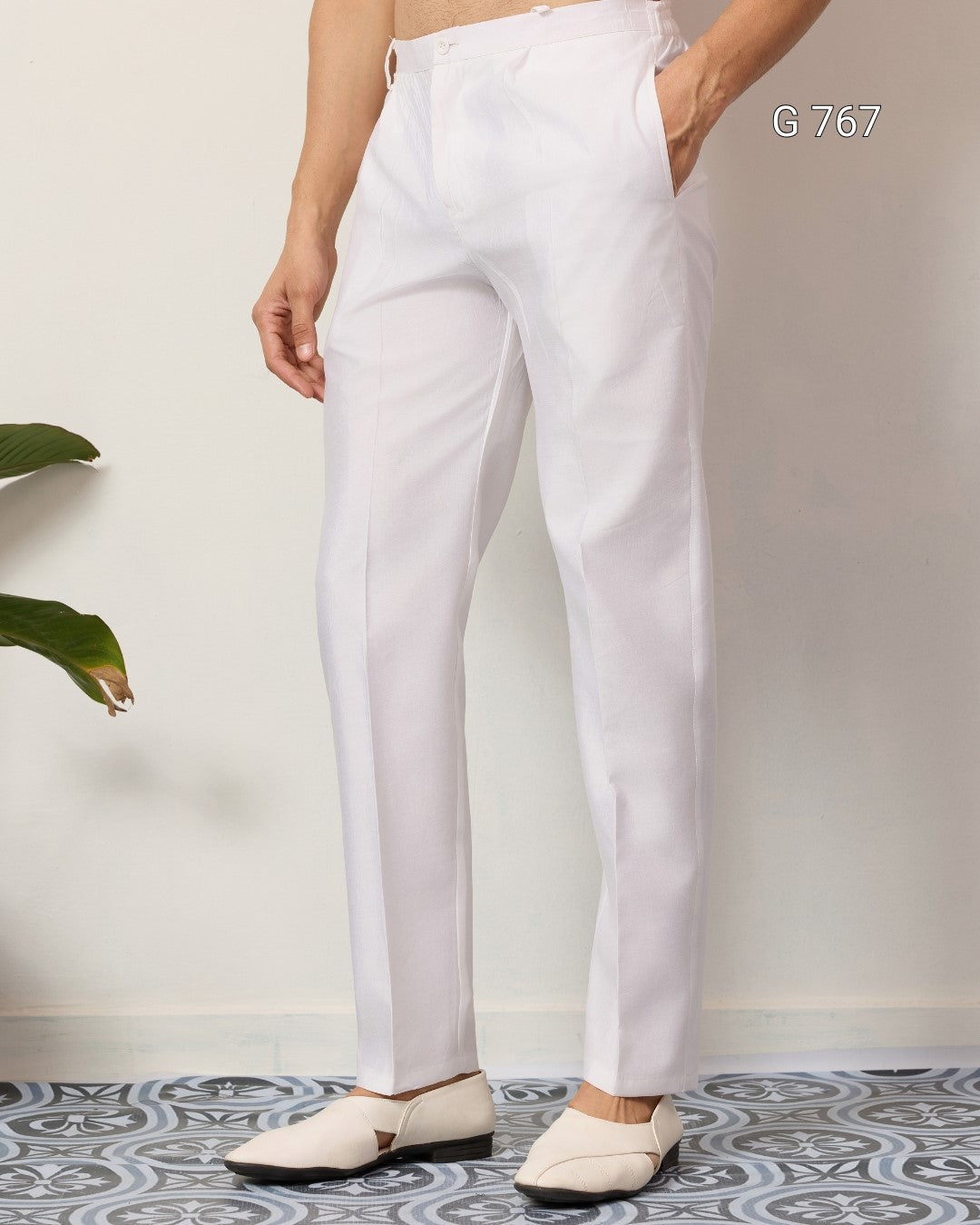 Person wearing white pants standing on a patterned floor with a plant in the corner.
