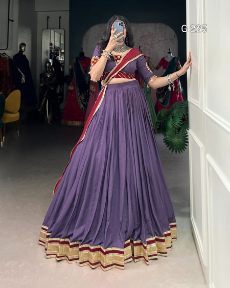 Person wearing a purple saree with red and gold border in a room.