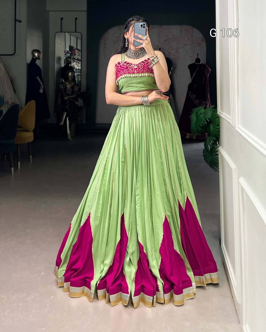 Person wearing a green and pink saree with a matching blouse in a room.