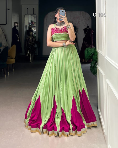 Person wearing a green and pink saree with a matching blouse in a room.