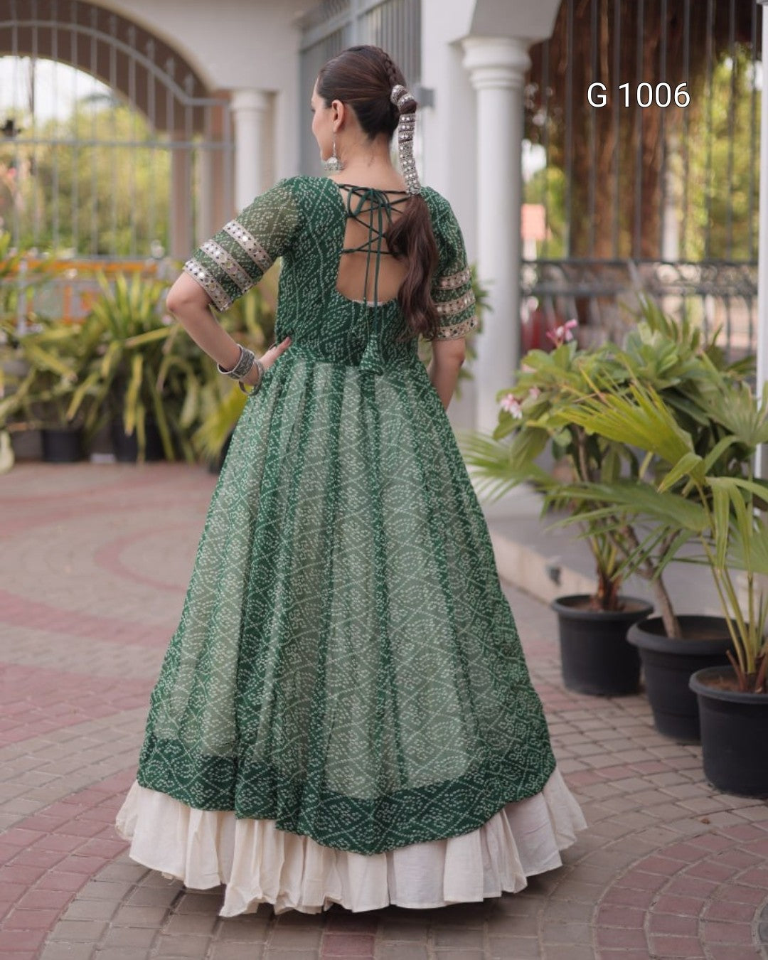 A woman wearing a green embroidered Anarkali gown with a cream under-skirt, photographed from the back in an outdoor courtyard setting. The text 'G 1006' is visible in the top right corner.