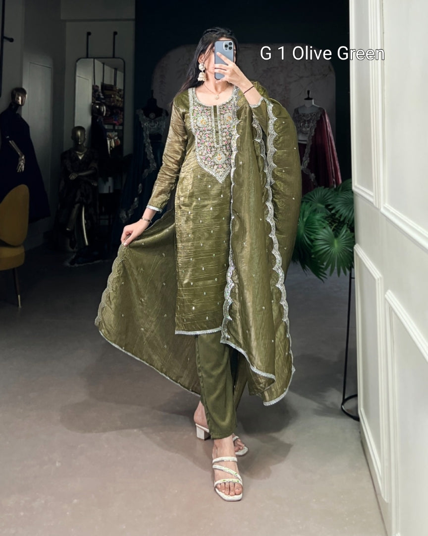 Woman wearing an olive green traditional outfit with embroidery, standing in a room.