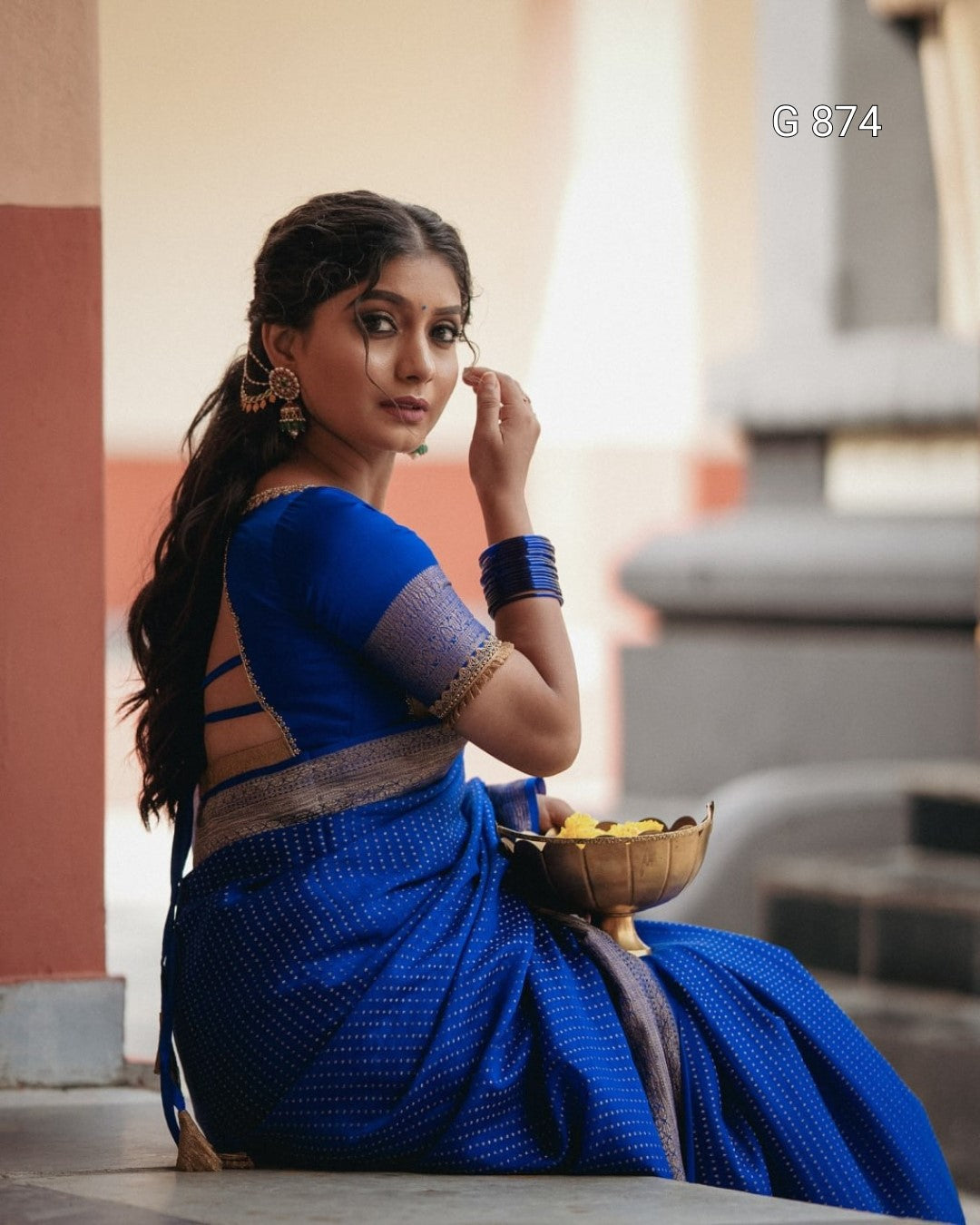 Woman in a blue saree sitting on steps with a blurred background