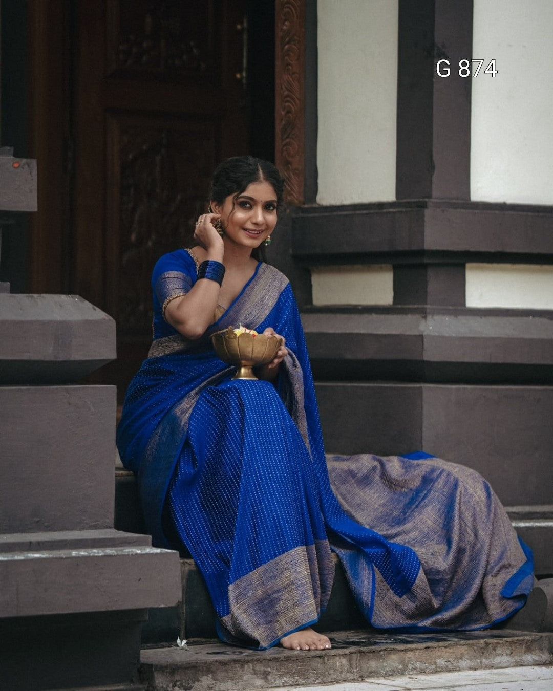 Woman in a blue saree sitting on steps holding a bowl.