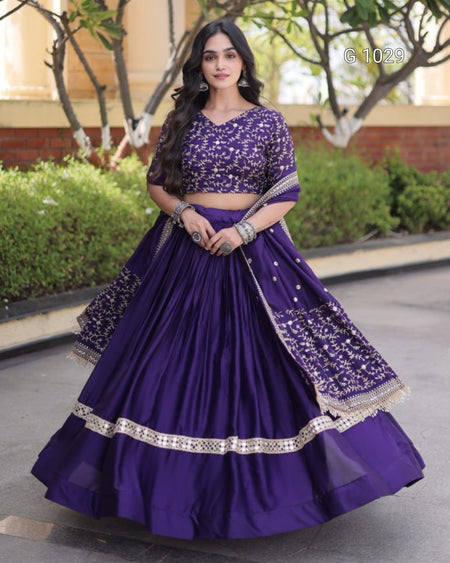 A woman modeling a purple Indian ethnic wear set consisting of a flared skirt, embroidered crop top, and matching dupatta, standing outdoors.
