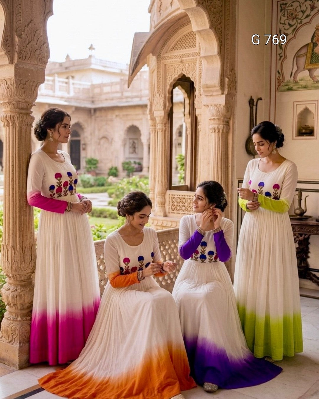 Four women in colorful traditional dresses sitting on a marble floor with ornate architecture in the background.