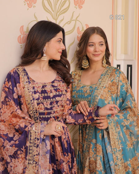 Two women in traditional outfits with floral patterns standing against a decorative wall.