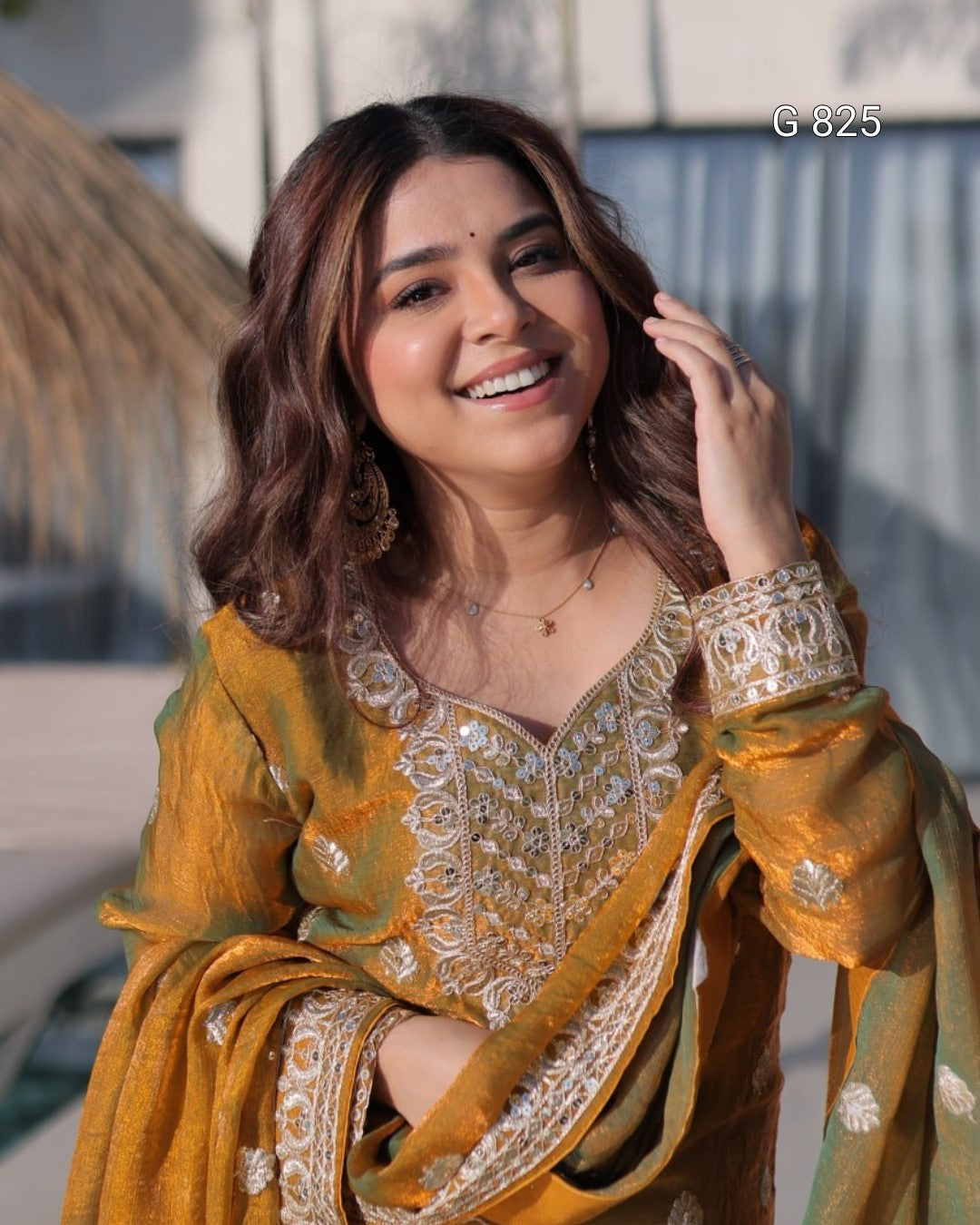 Woman in traditional yellow and green outfit with intricate patterns, standing outdoors.
