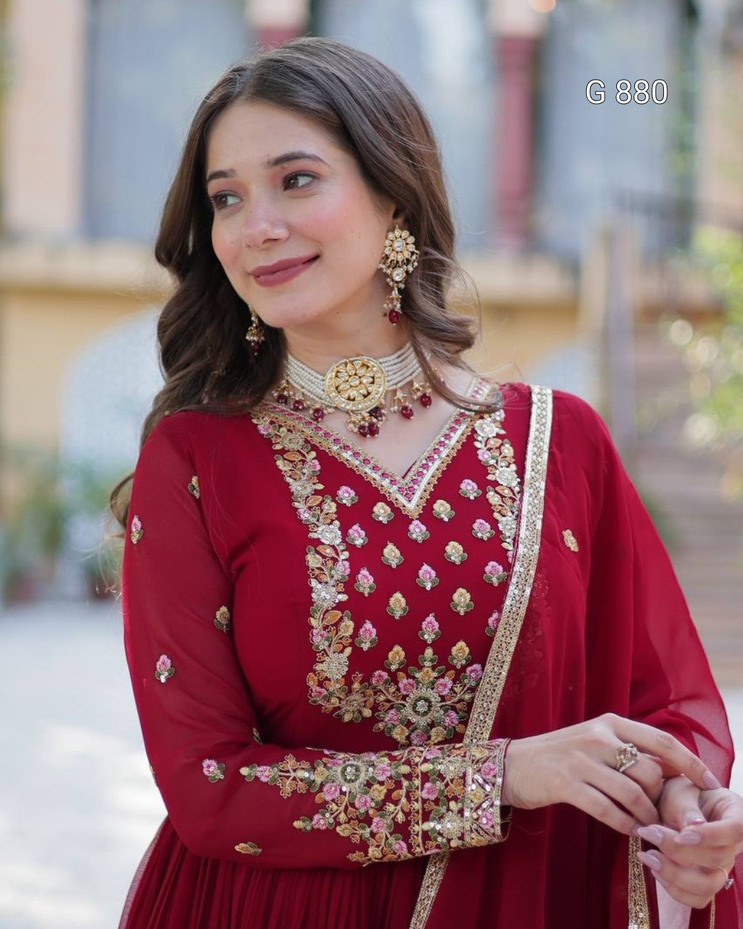 Woman wearing a red embroidered traditional outfit with gold jewelry.