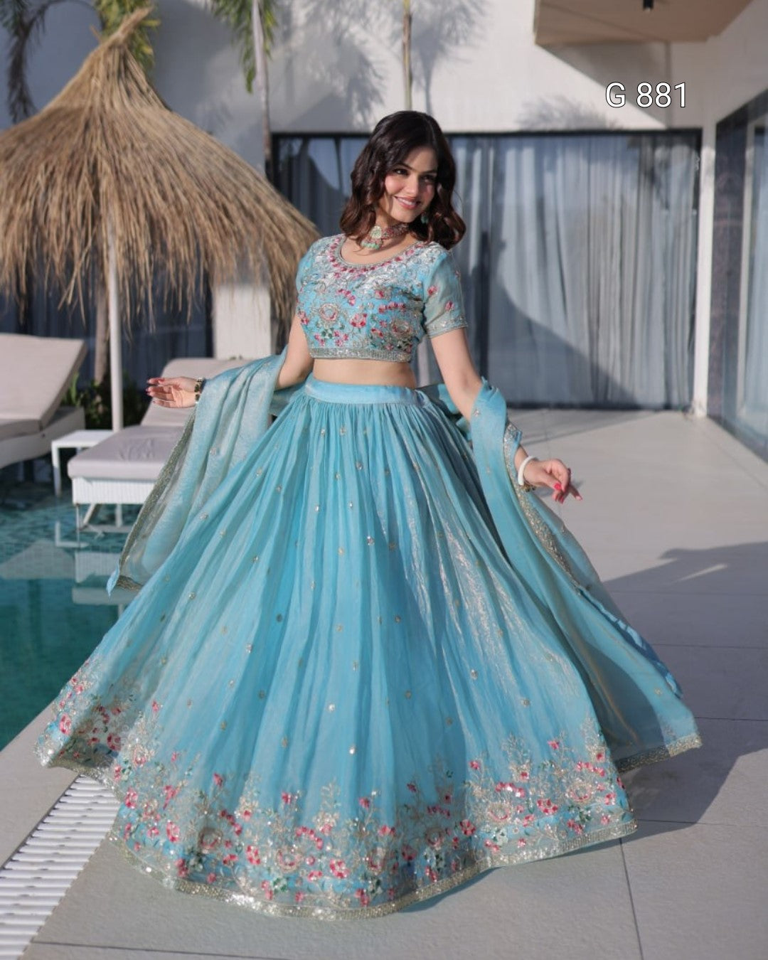 Woman in a light blue embroidered traditional outfit by a poolside.