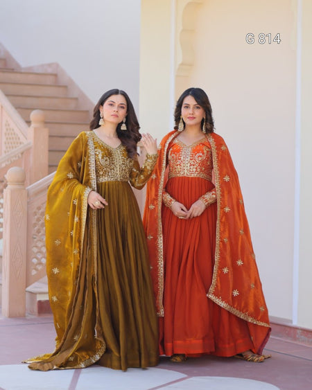 Two women in traditional embroidered sarees standing in a decorative indoor setting.