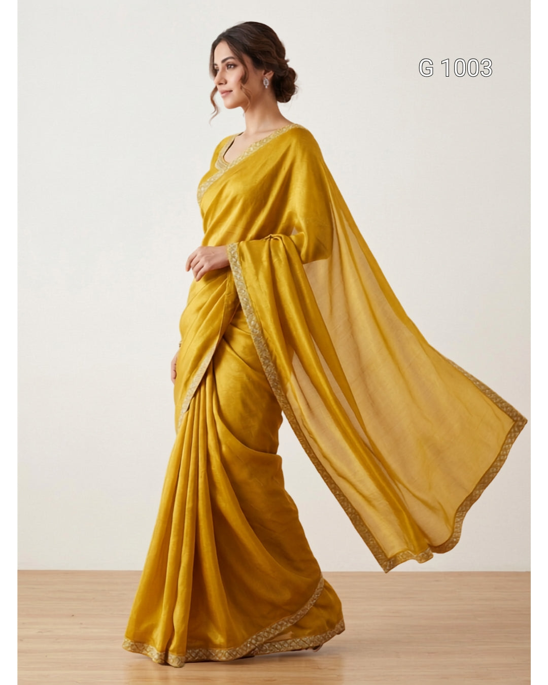 A woman modeling a mustard yellow saree with gold border detailing, standing in profile against a plain off-white studio background.
