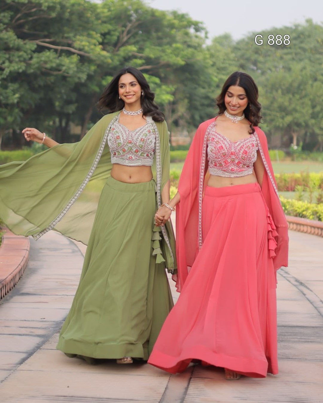 Two women in traditional green and pink sarees standing outdoors with trees in the background.