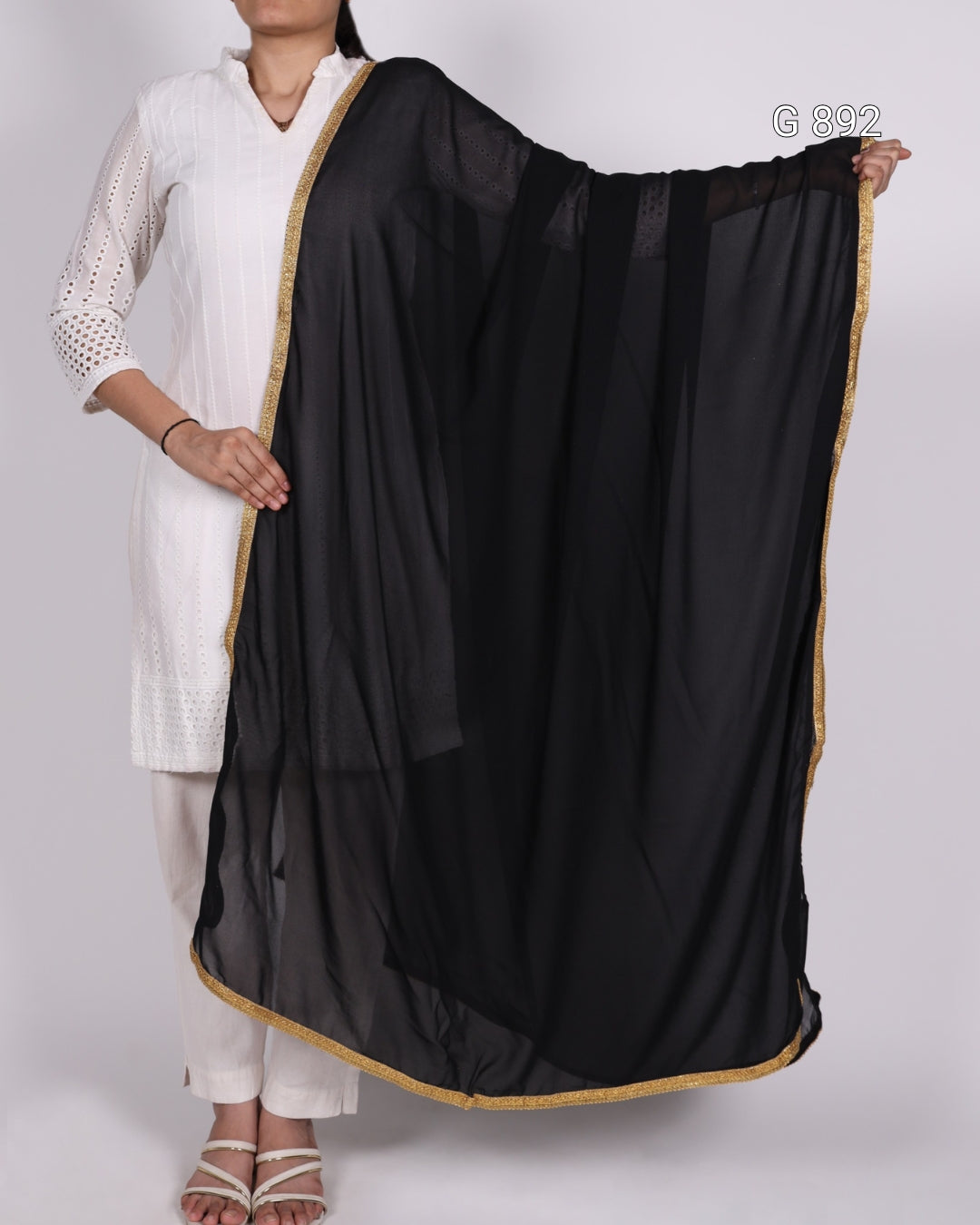 Person wearing a black dupatta with gold border draped over one shoulder on a white background