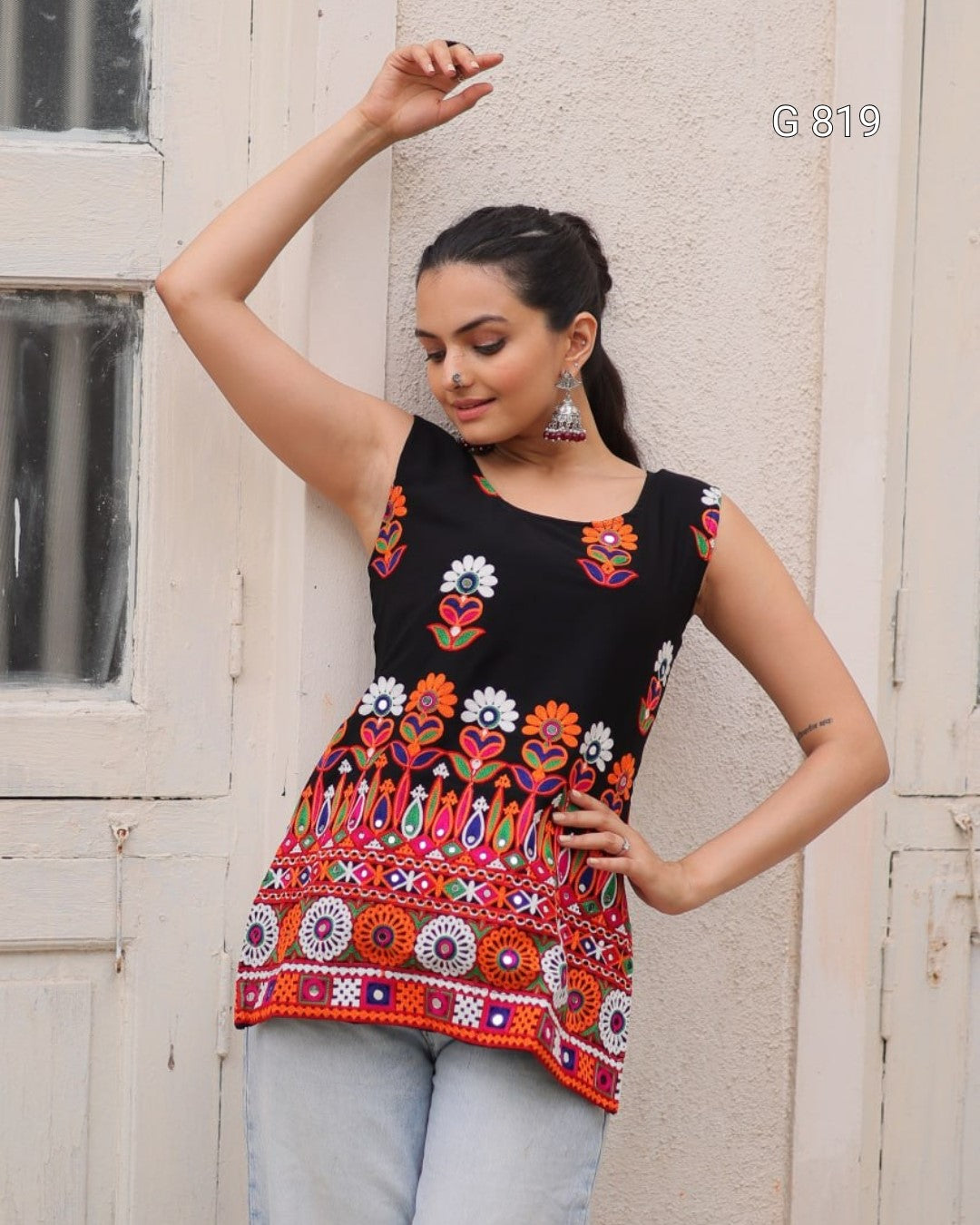 Woman wearing a black sleeveless top with colorful floral patterns against a beige wall.