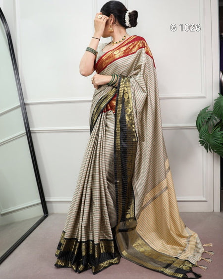 A woman models a traditional Indian saree in a studio setting. The saree has a beige and black striped body with a red and gold border, and a matching red and gold border on the blouse.