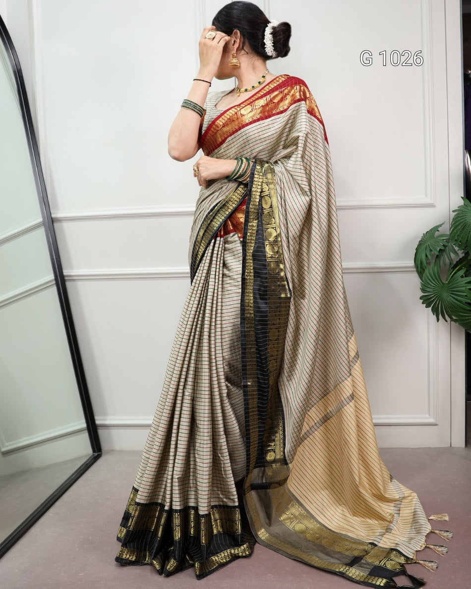 A woman models a traditional Indian saree in a studio setting. The saree has a beige and black striped body with a red and gold border, and a matching red and gold border on the blouse.