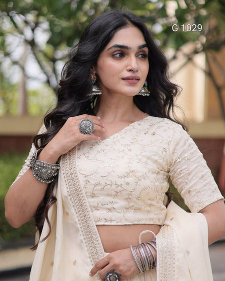 A woman wearing a cream-colored embroidered traditional outfit with a matching dupatta, silver-toned jewelry, and a visible 'G 1029' text overlay in the top right.