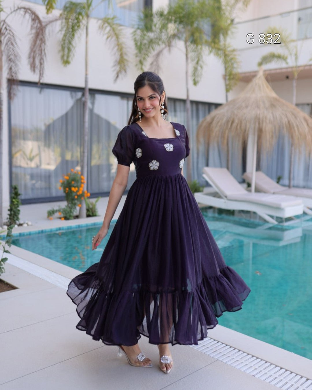 Woman in a purple dress standing by a pool with a building and plants in the background