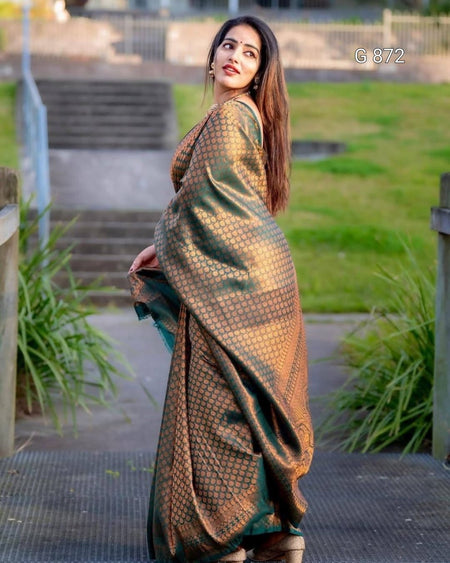 Woman in a green and gold saree standing outdoors with grass and steps in the background