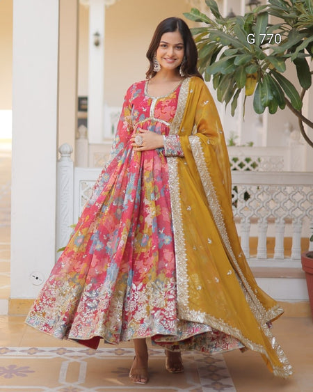 Woman in a floral dress and yellow dupatta standing indoors with decorative elements.