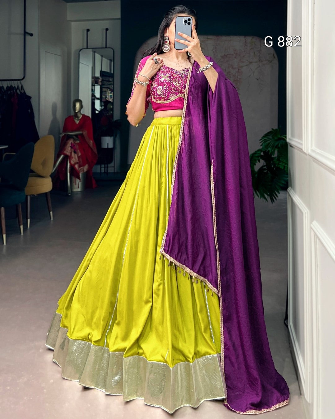 Person wearing a bright yellow and pink traditional outfit with a purple dupatta in a room.