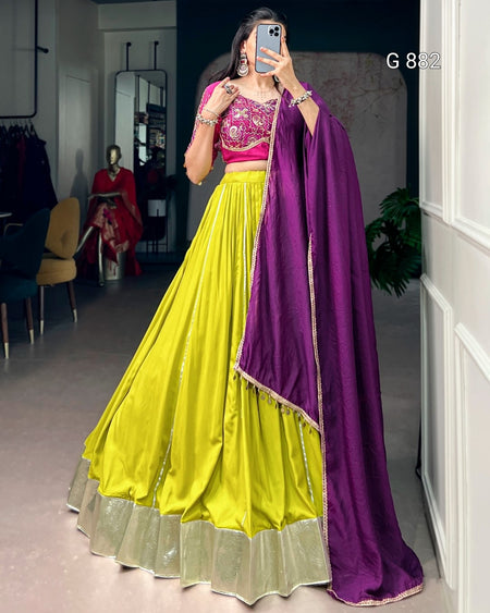 Person wearing a bright yellow and pink traditional outfit with a purple dupatta in a room.
