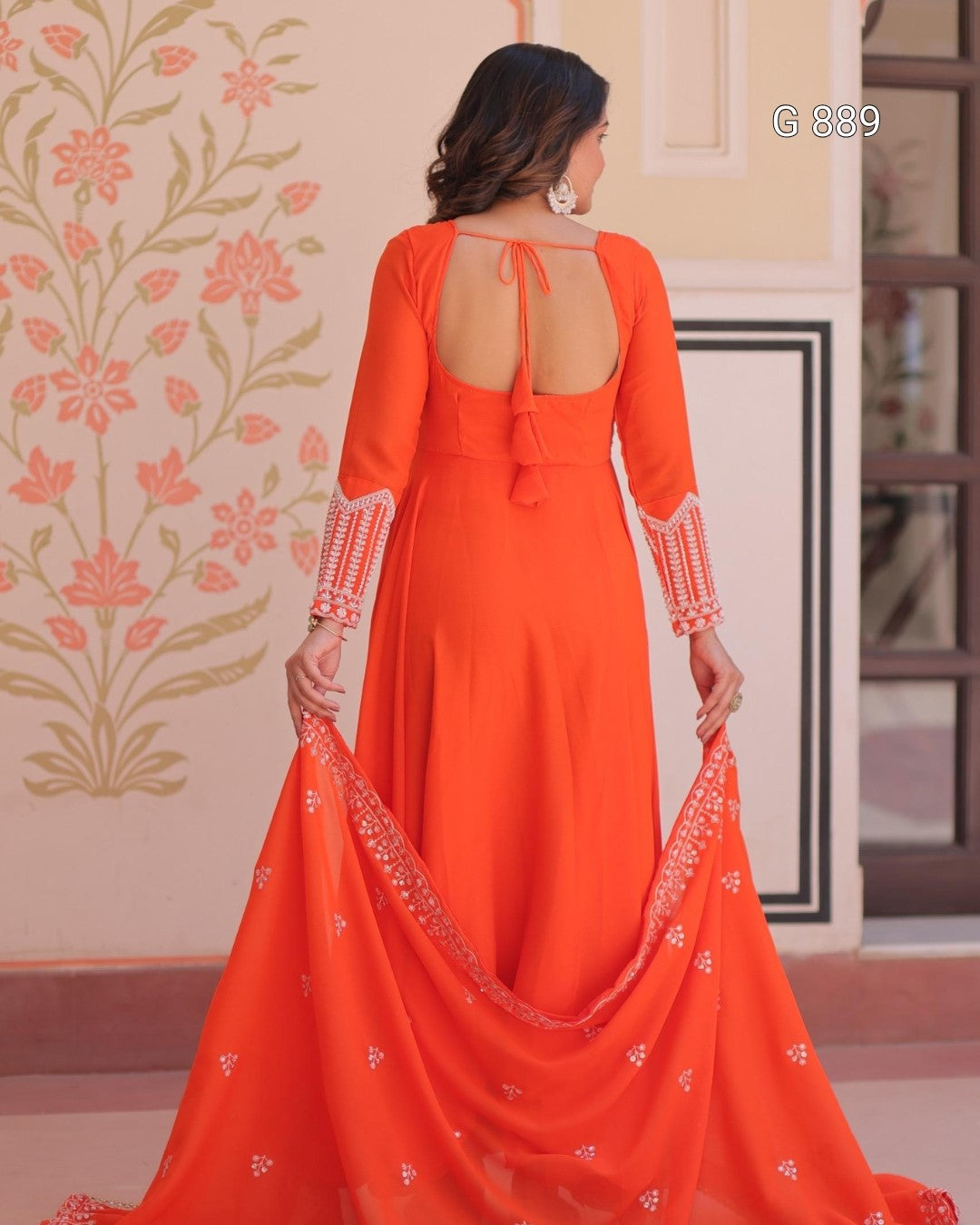 Woman wearing an orange dress with a floral patterned wall in the background