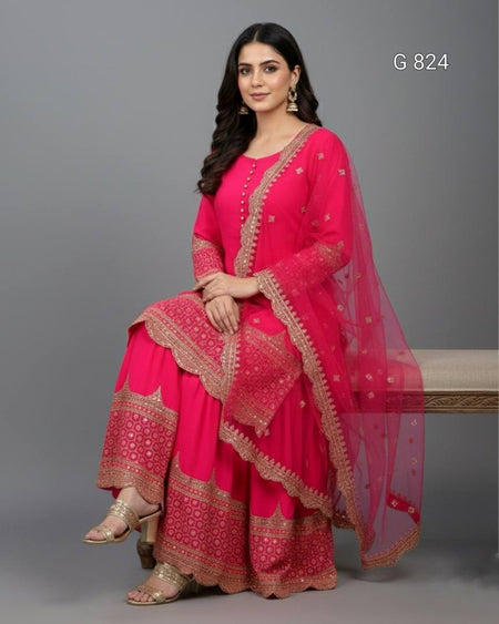 Woman wearing a bright pink traditional outfit with gold embroidery on a gray background