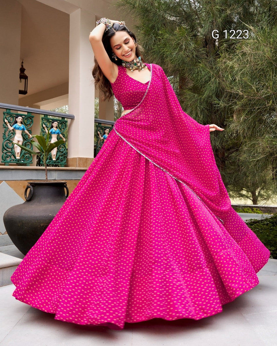 A woman wearing a bright pink traditional dress with white polka dots and a matching draped scarf, standing outdoors in front of a building and trees. The number 'G 1223' appears in the top right corner.