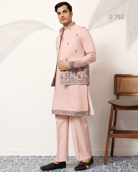 Man wearing a traditional pink outfit with embroidery, standing against a white wall with a wooden chair.