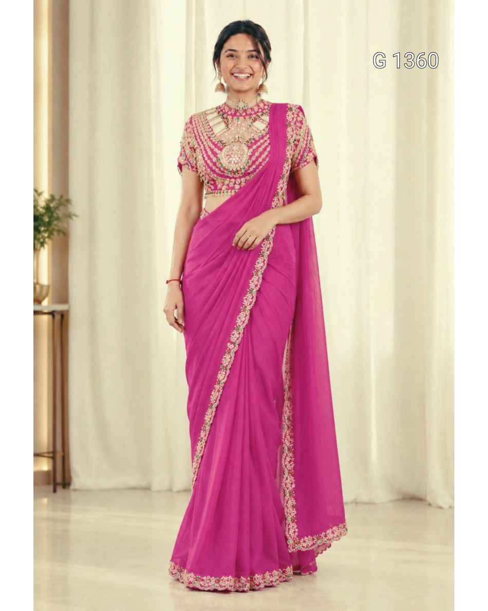 A woman modeling a bright pink sari with gold floral embroidery along the border and a matching embroidered blouse, standing in front of a cream-colored curtain backdrop.