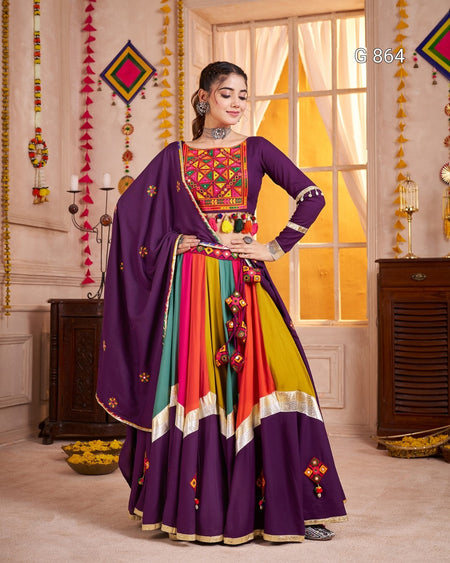 Woman in a colorful traditional outfit with a vibrant purple dupatta in a decorated room.