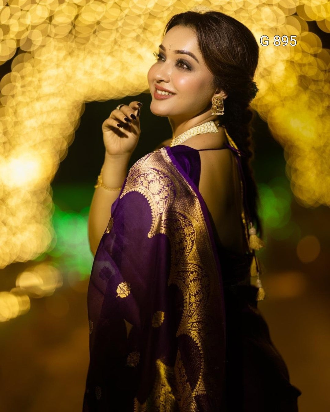 Woman in a purple saree with gold patterns against a blurred light background