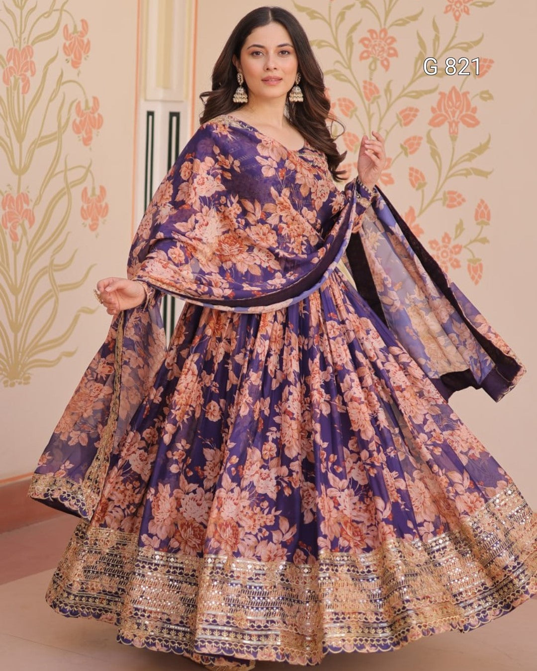Woman wearing a floral dress with a matching shawl against a decorative wall.