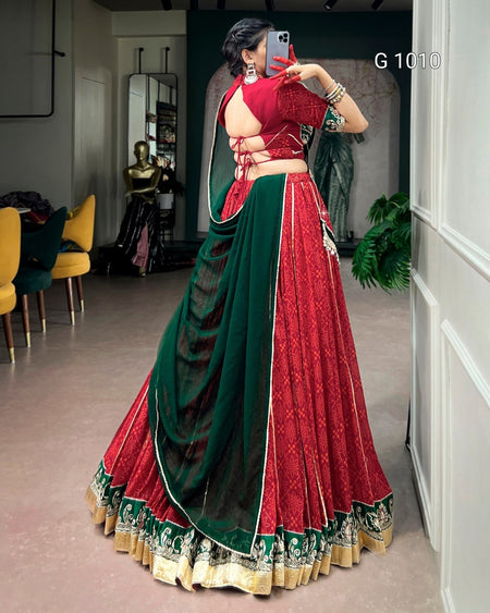 A woman takes a mirror selfie in a boutique wearing a traditional Indian lehenga choli dress. The dress features a deep red skirt and blouse with intricate gold embroidery, paired with a dark green dupatta and a matching green embroidered border on the skirt.