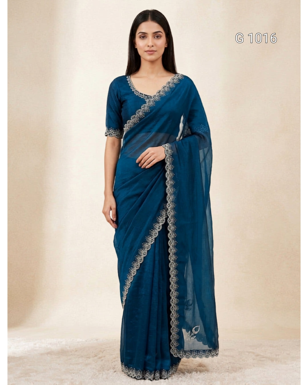 A woman modeling a teal blue saree with silver embroidered borders, standing against a neutral beige studio backdrop. The number 'G 1016' is printed in the top right corner.
