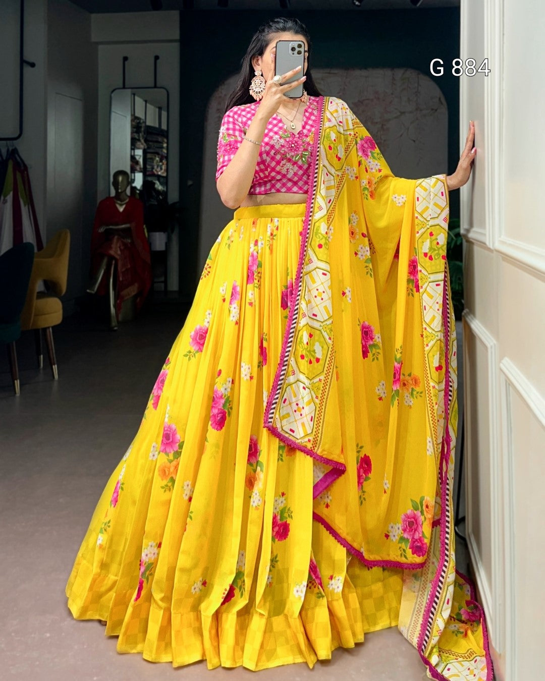 Person wearing a yellow saree with pink blouse in a room.