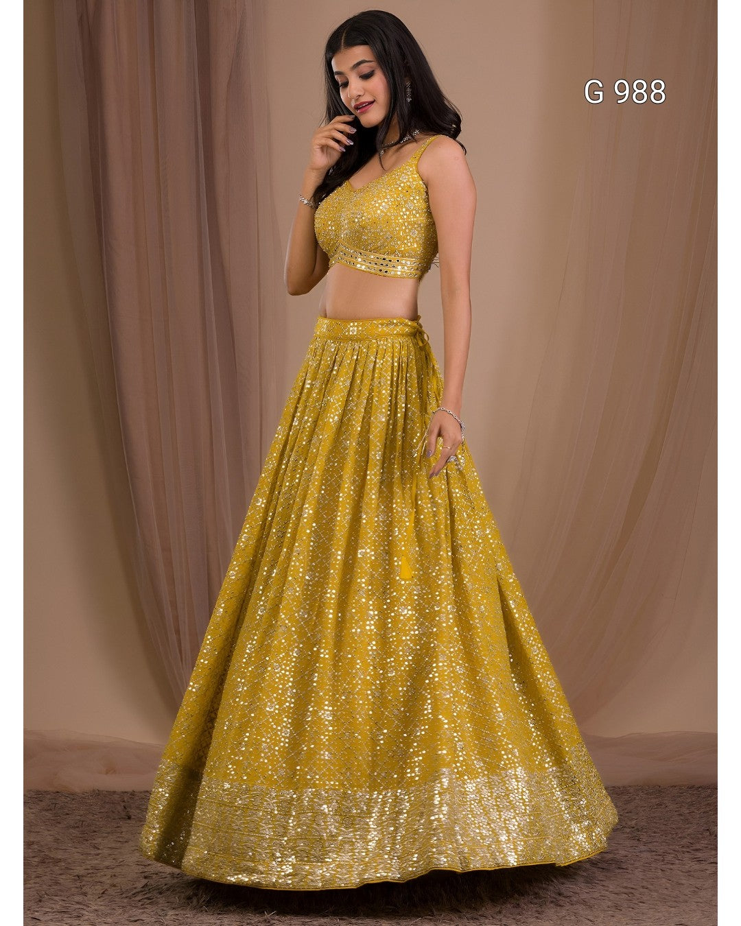 A woman modeling a bright yellow-gold sequined two-piece traditional outfit with a sleeveless crop top and a full flared skirt, posed against a draped beige studio backdrop. The text 'G 988' appears in the top right corner.