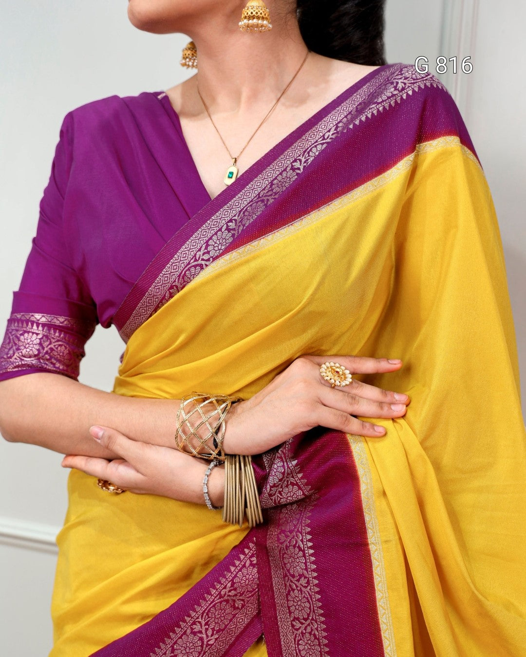 Woman wearing a yellow and purple saree with jewelry, against a white background.